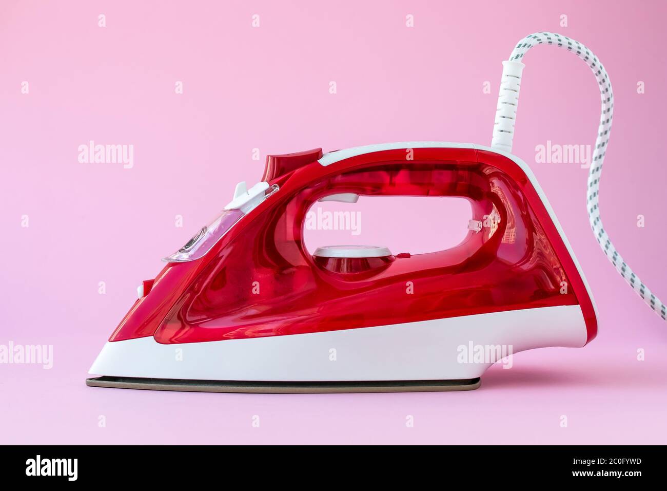 Red plastic iron on pink background. Appliance for ironing clothes, housework concept Stock Photo