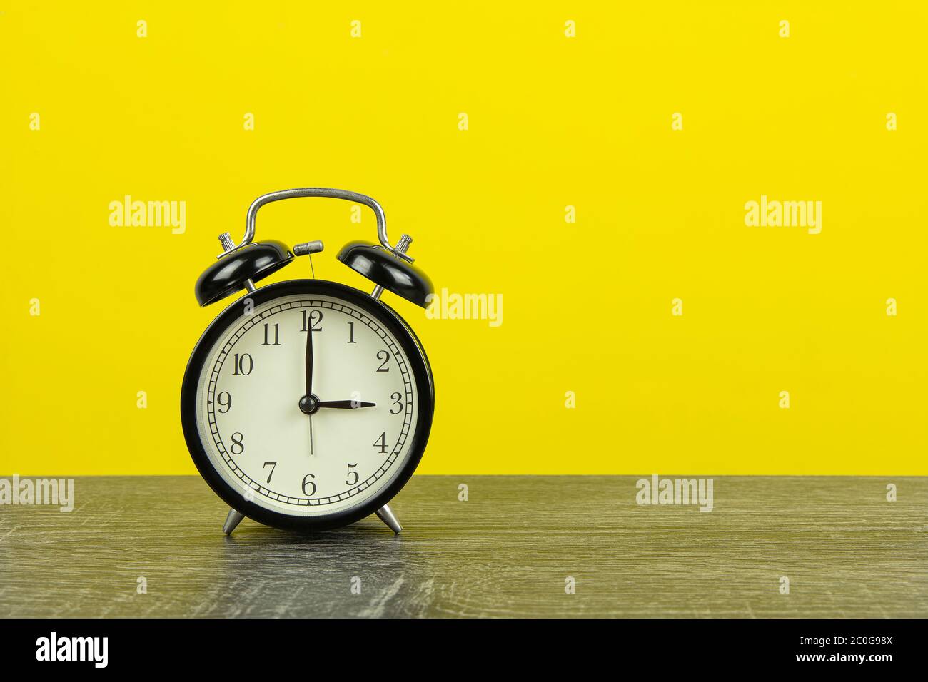 Black retro alarm clock on wooden table and yellow background. Stock Photo