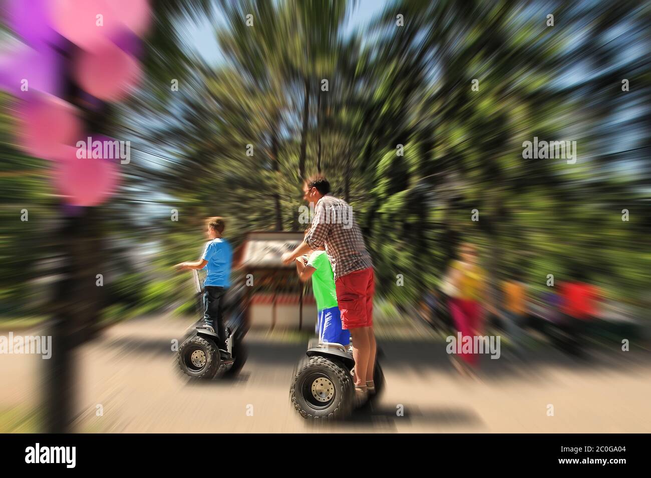 Abstract background. Father and children riding a Segway in the park.  Blur effect defocusing filter applied. Stock Photo