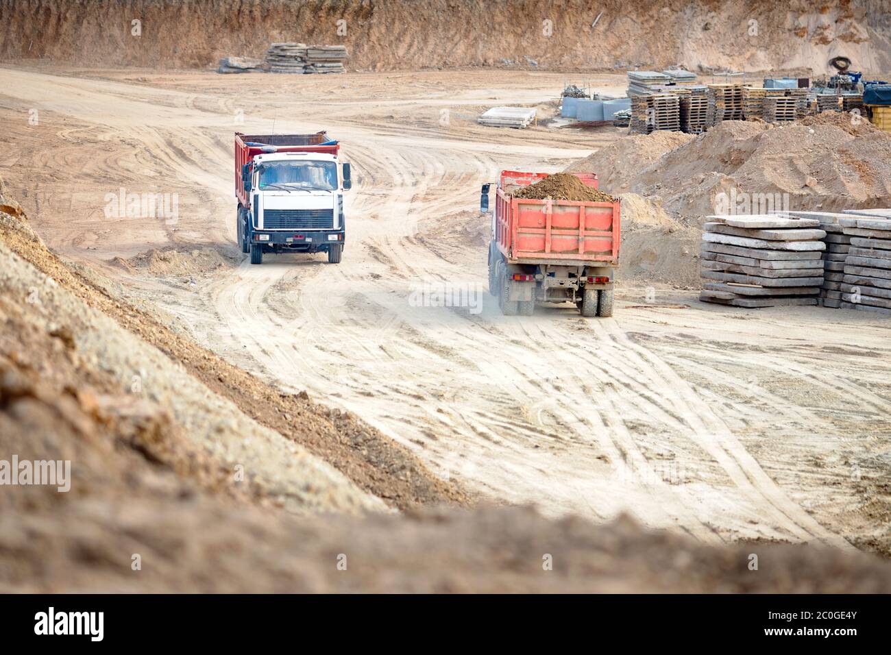 Two multi-ton heavy mining dump trucks empty and loaded during removal of construction soil from construction site. Concept of providing transport Stock Photo