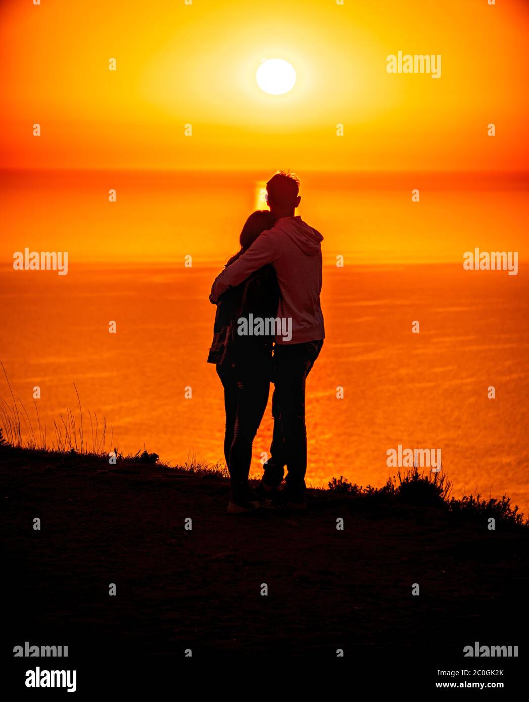 A red burning sunset over the sea with the silhouette of a young couple ...