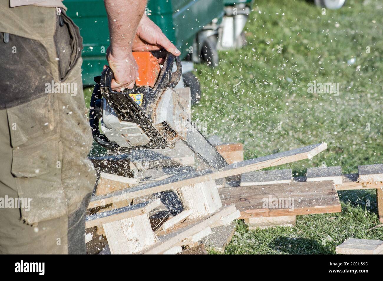 A man using a chainsaw to cut through wooden pallets with sawdust spraying . Stock Photo