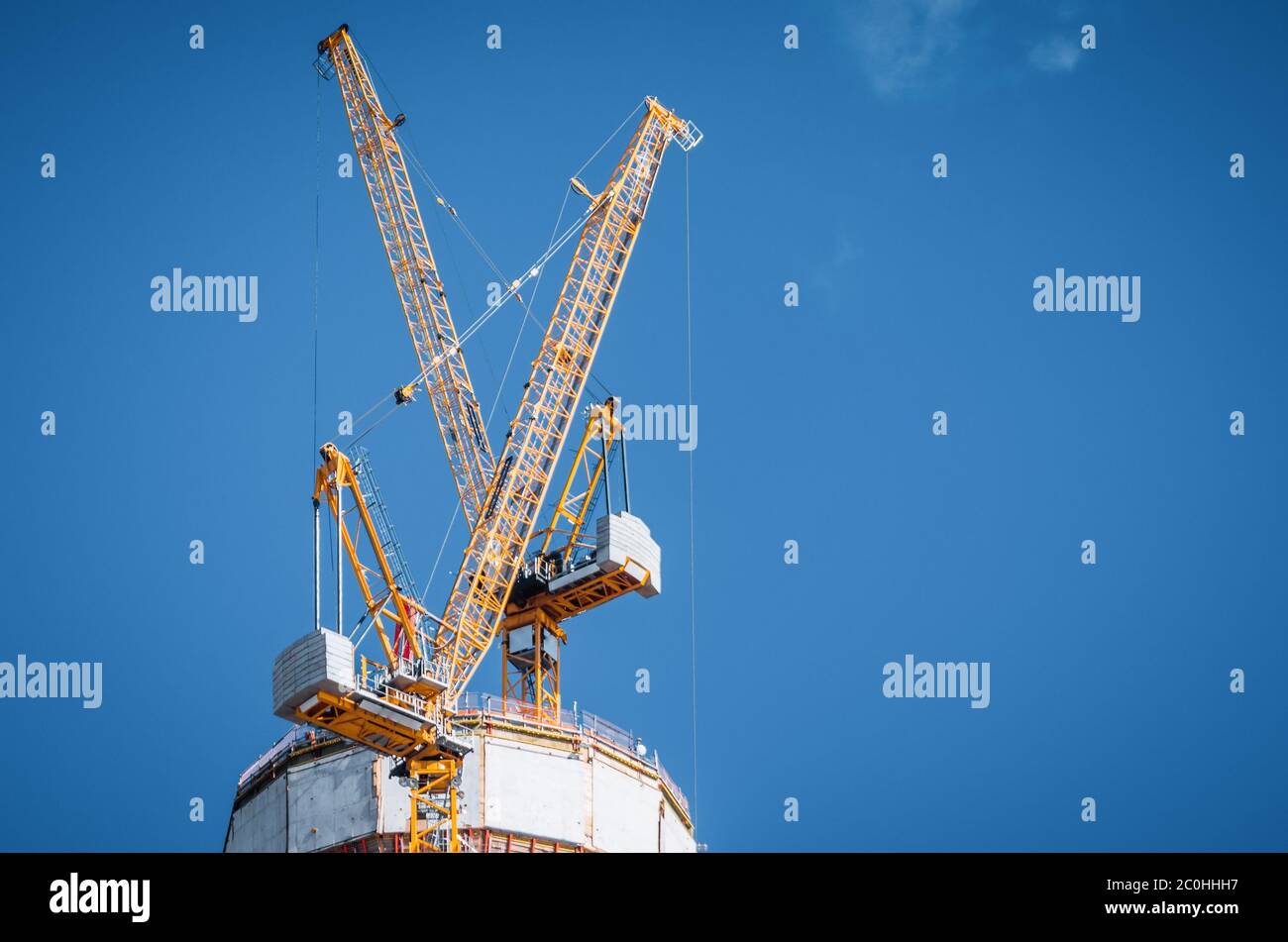 Two yellow cranes on top of a skyscraper under construction on a blue ...