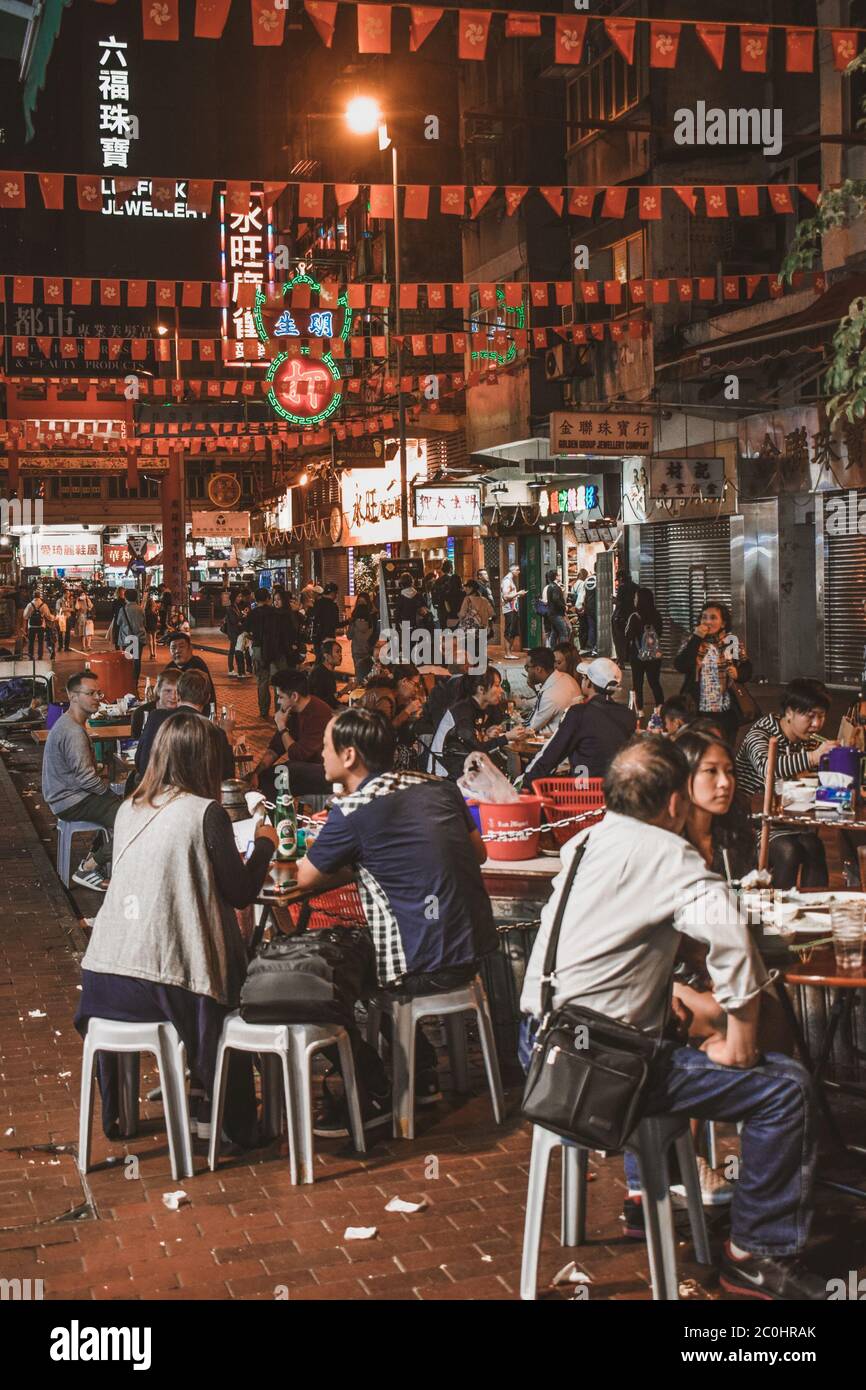 People sitting and eating street food at the evening Temple Street Market in Hong Kong Stock Photo