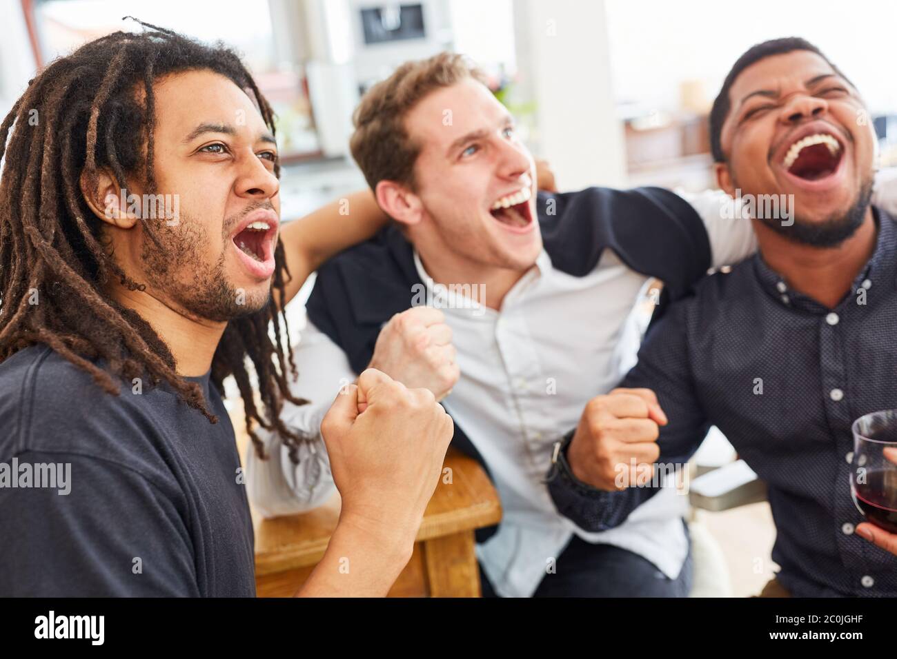 Friendly men cheer together while watching football at home Stock Photo