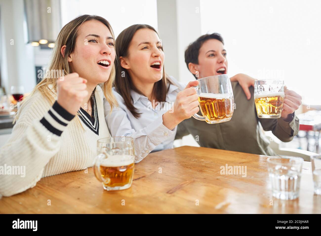 Group of women watch football and drink beer and cheer on their team Stock Photo
