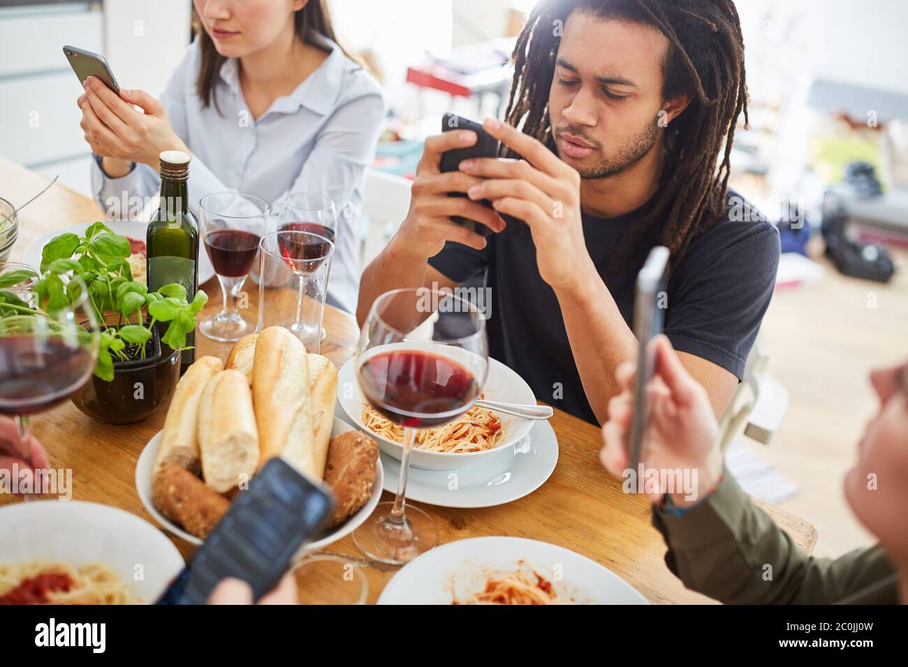 Friends look at social media websites on smartphone while eating at the table Stock Photo