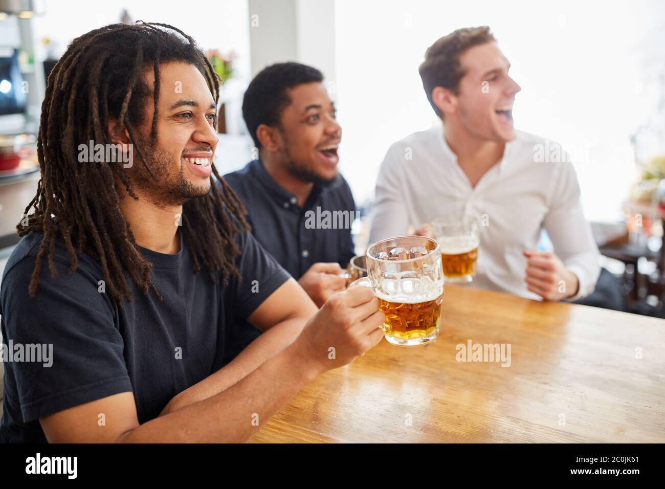 Three men as friends drink beer and watch a soccer game on TV together Stock Photo