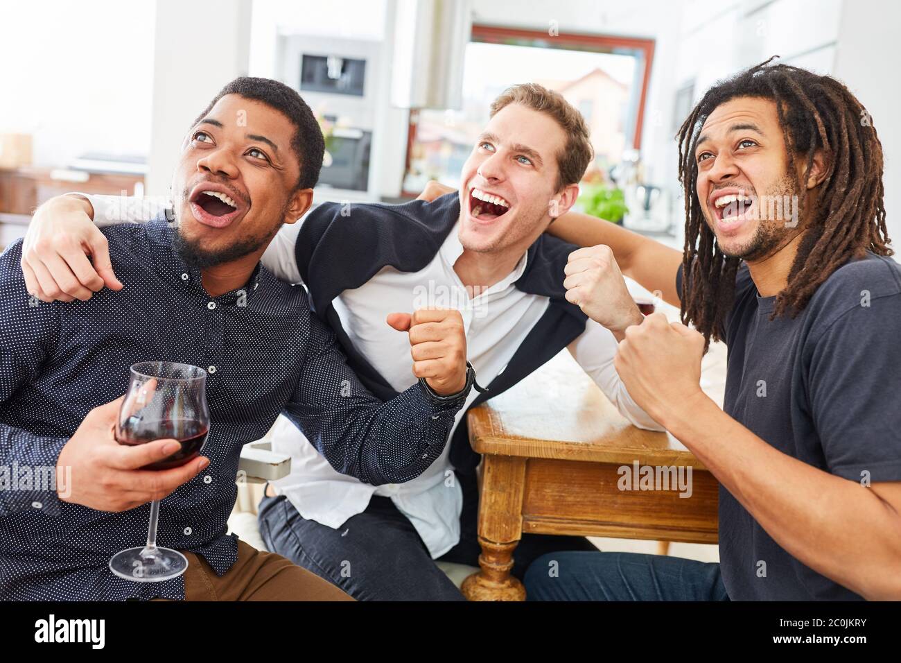 Friendly men cheer together while watching football or sport at home Stock Photo
