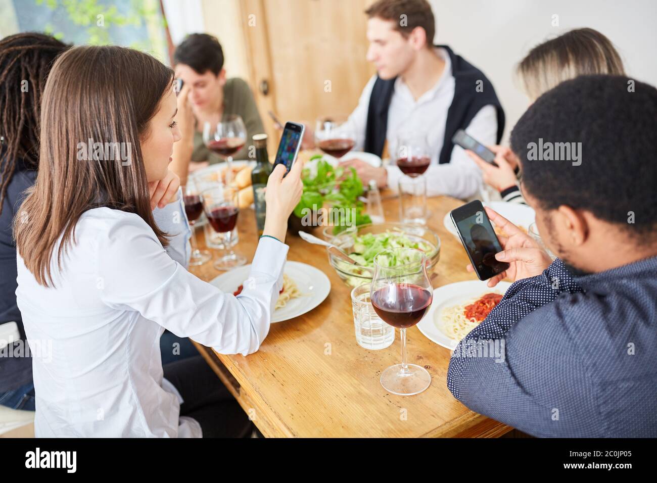 Distracted friends all look at their smartphone while having lunch together at the table Stock Photo