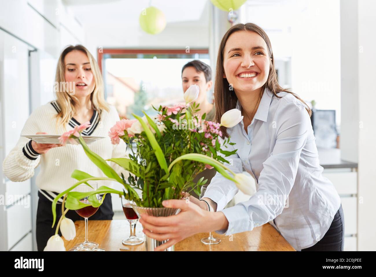 Woman decorating table with girlfriends and laying for lunch in shared kitchen Stock Photo