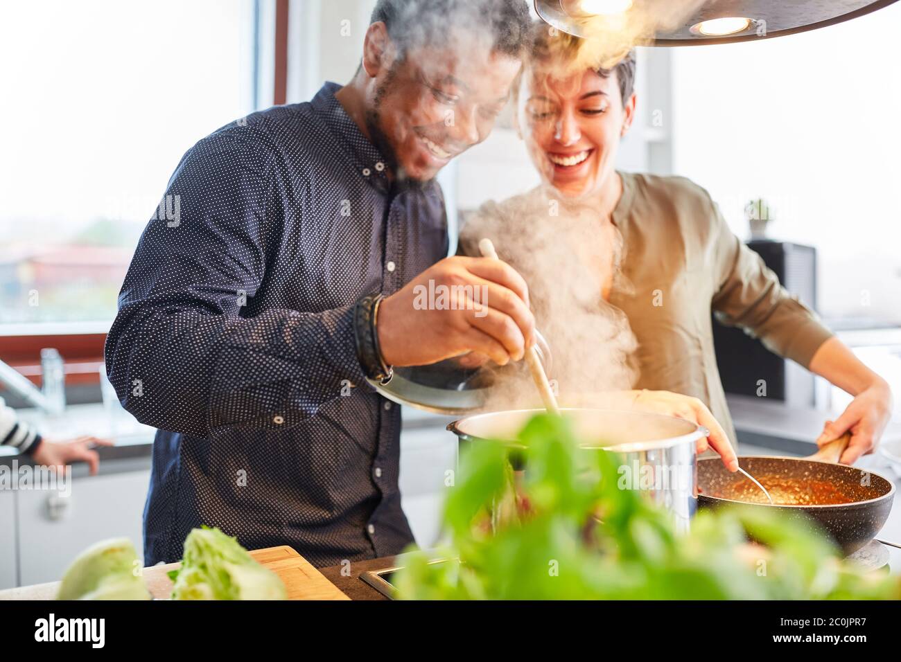 Happy friends or couple cooking food in kitchen for meal together Stock Photo