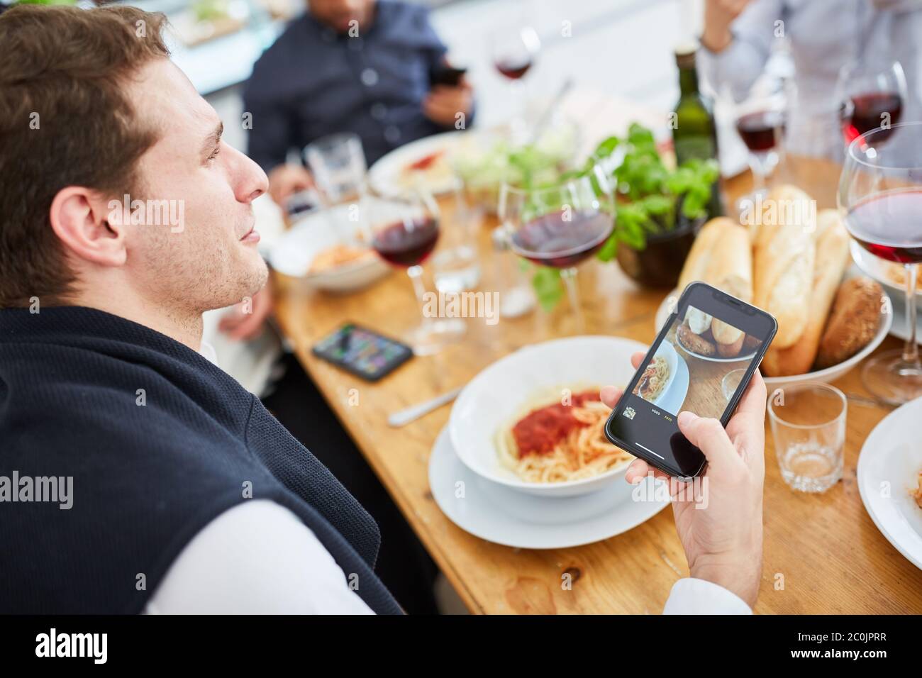 Man uses smartphone while eating pasta with friends at table Stock Photo