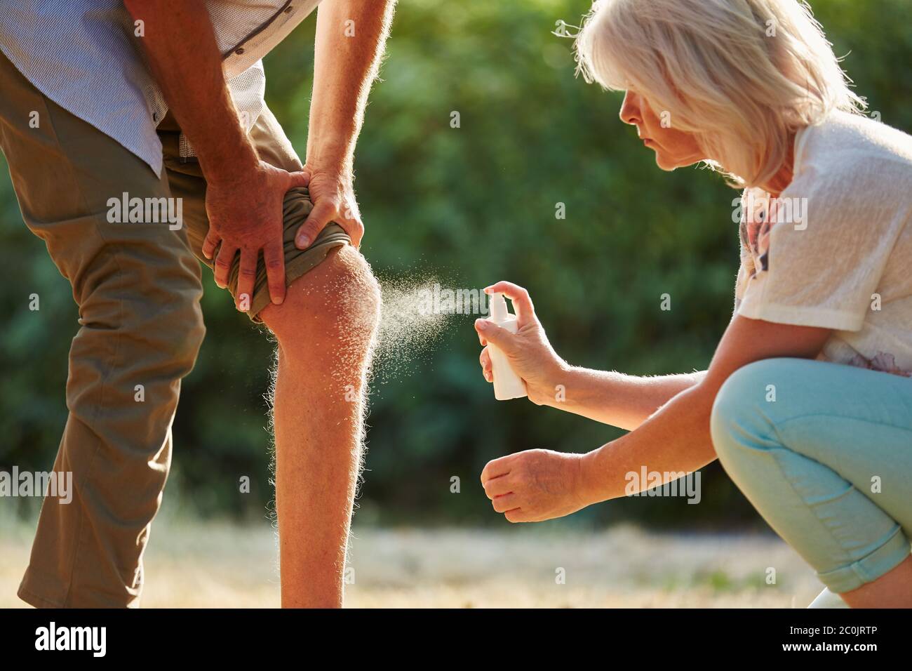 Man with knee injury in nature gets pain relief spray Stock Photo