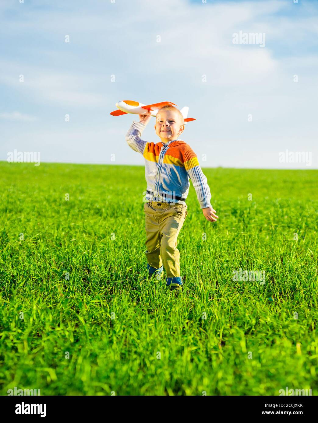 Happy boy playing with toy airplane against blue summer sky and green ...