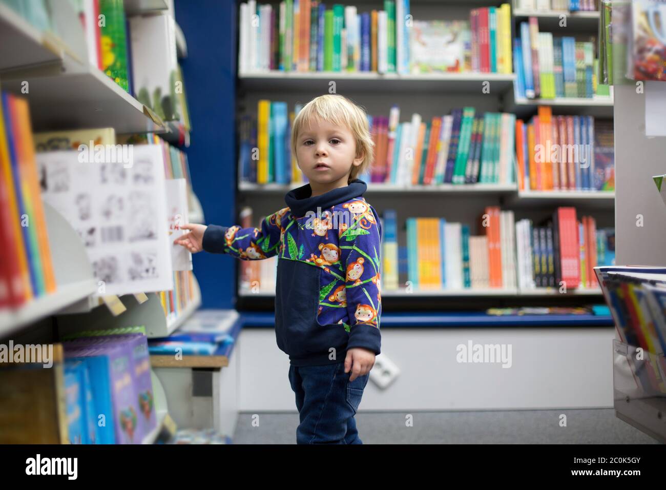 Adorable little boy, sitting in a book store and read book Stock Photo