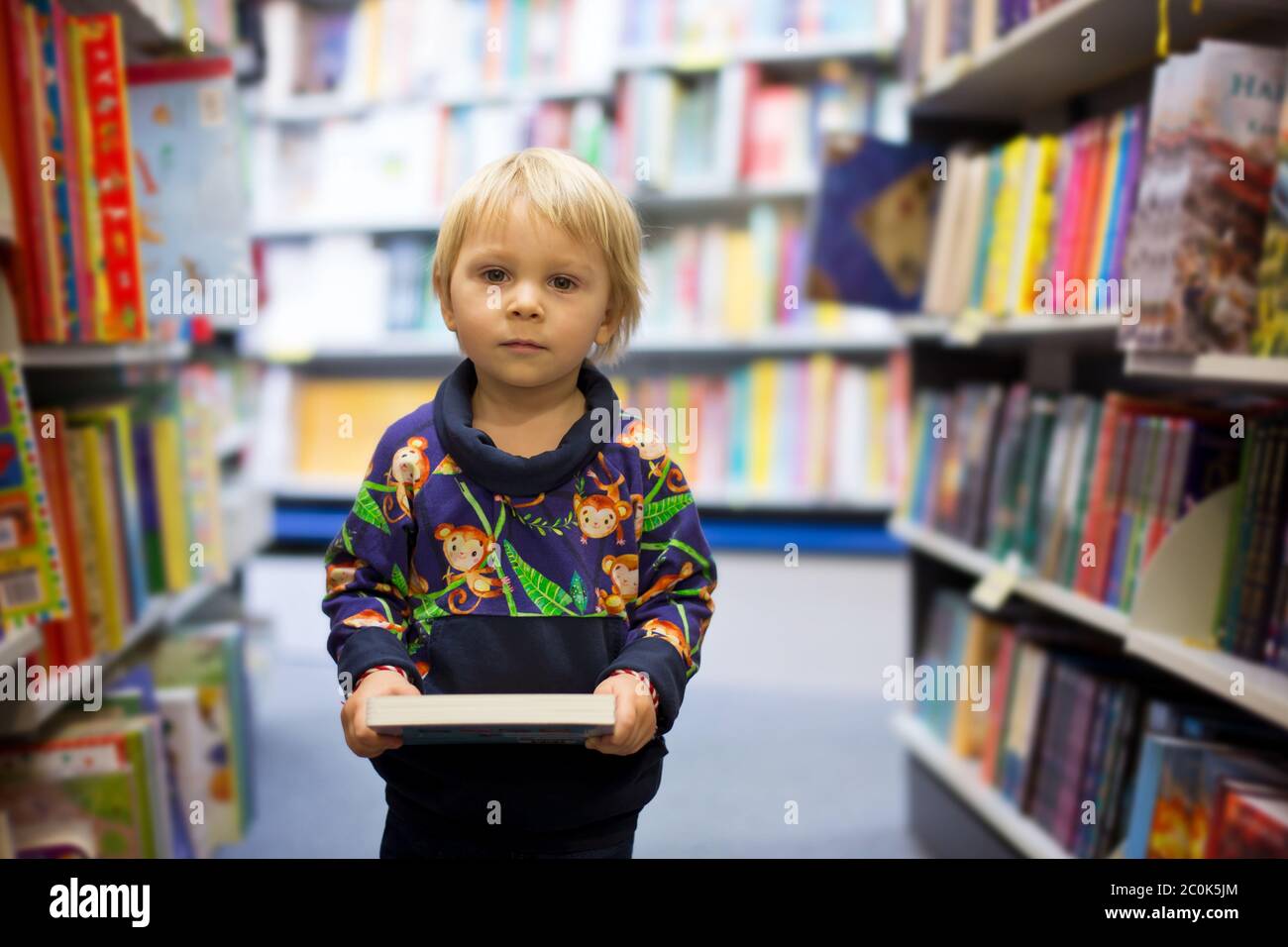 Adorable little boy, sitting in a book store and read book Stock Photo