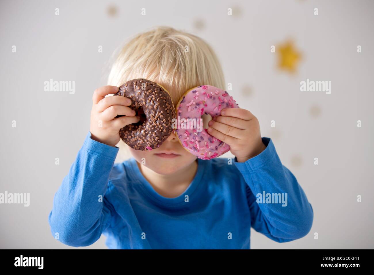 Cute sweet blonde child, playing and eating donuts at home Stock Photo