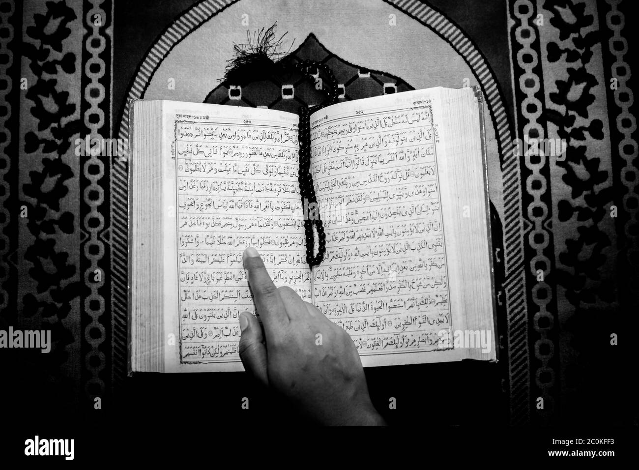 Muslim woman reading the Holy Quran using the finger. The Holy Quran on the mat of prayers . Top angle views. Indoors. Stock Photo