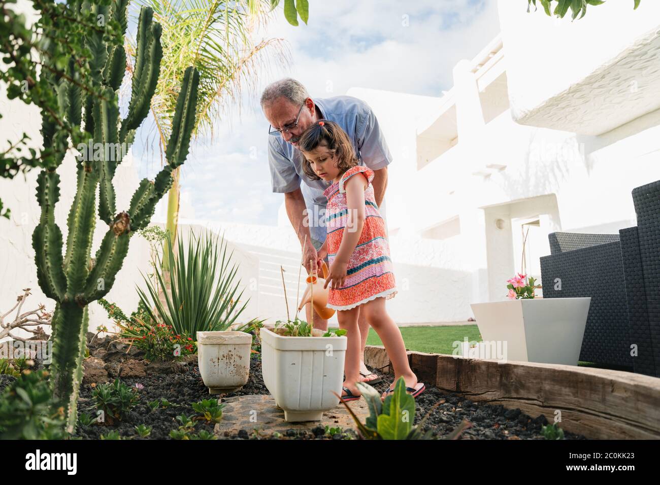 Retirement grandfather and granddaughter in backyard garden together, holding watering can have fun plants. Two generation good time spend outdoor Stock Photo