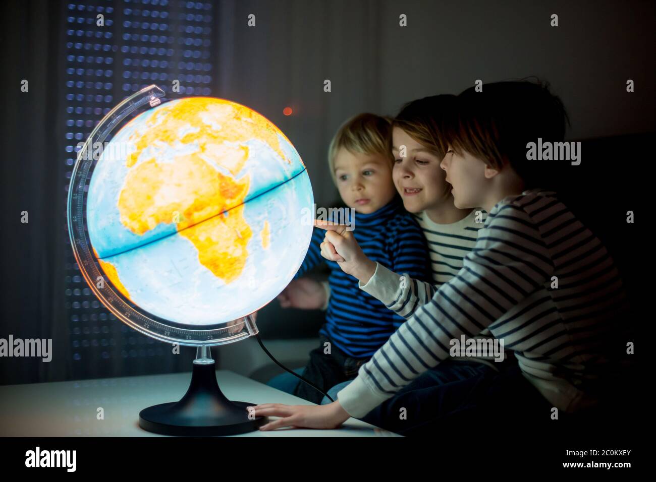 Little children, brothers, looking at illuminated globe, exploring the 