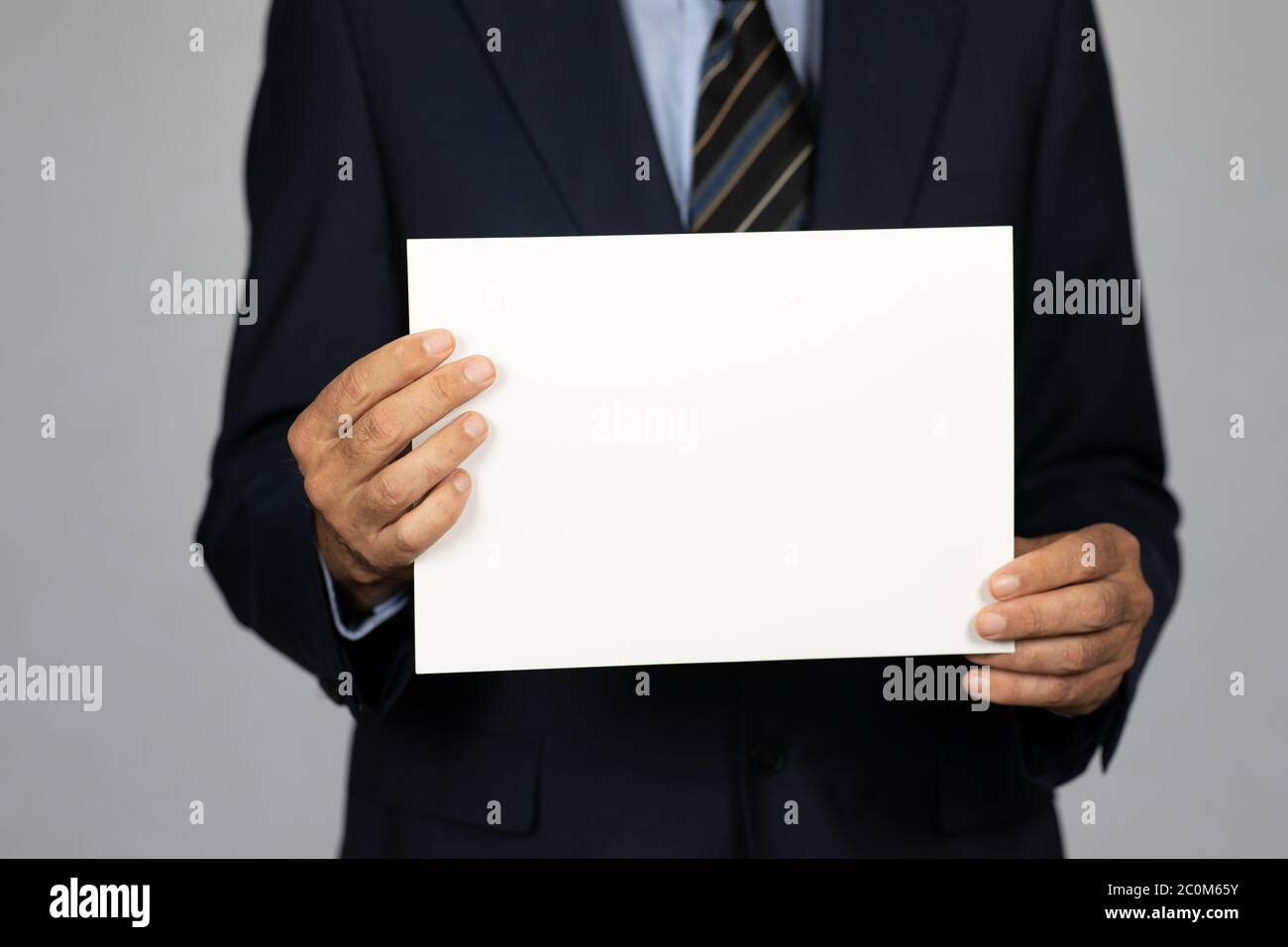 Businessman in suit holding an empty paper in front of him. Selective focus on foreground. Stock Photo