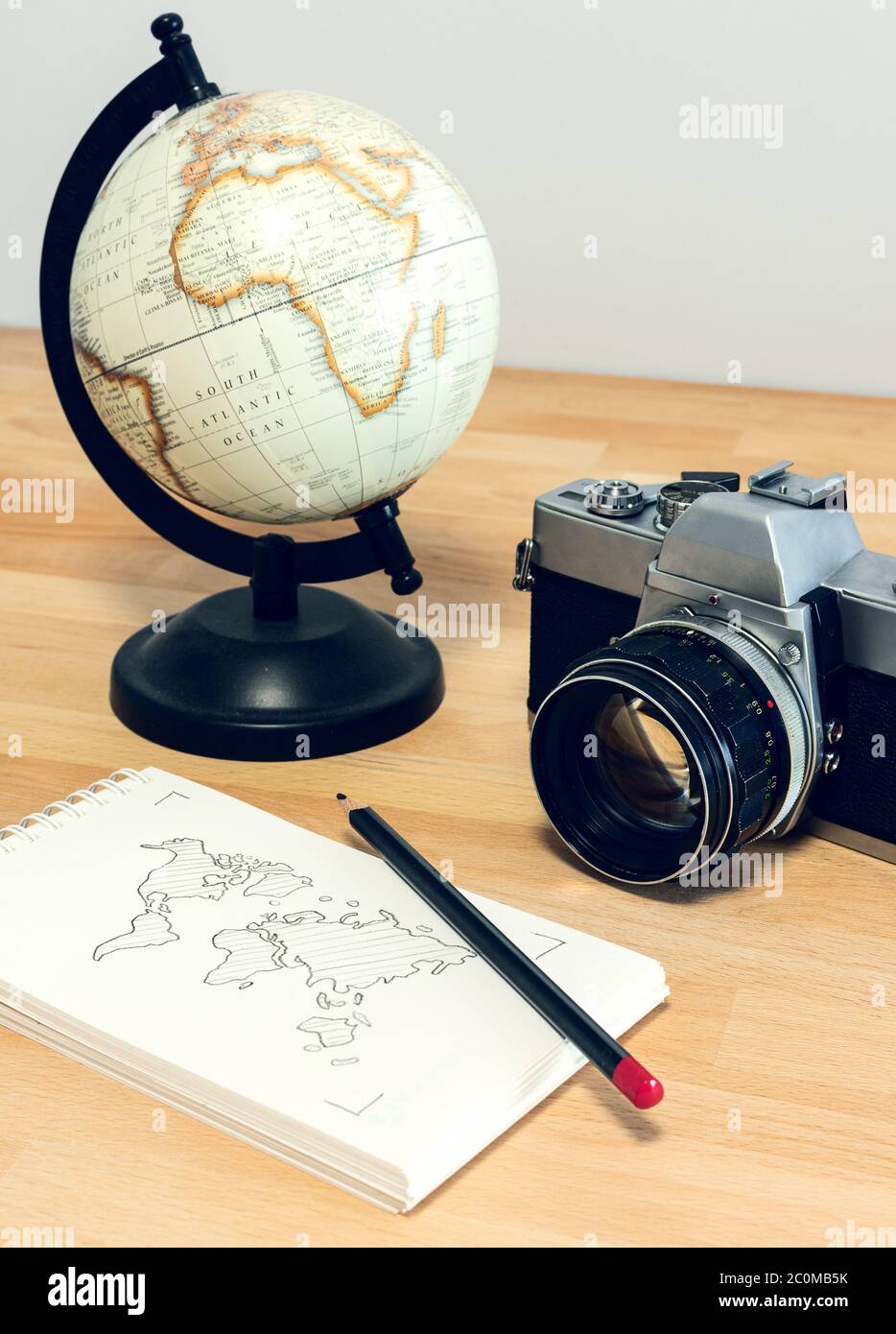 Camera, world globe and notebook with world map on a wooden desk. Travel concept image: planning a journey. Stock Photo