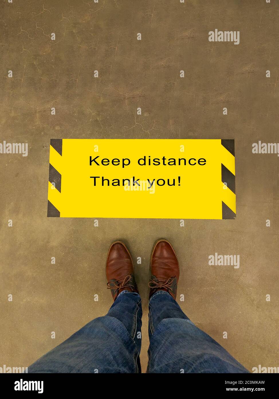 Man standing on the floor against a yellow line with the words keep distance in the shop. Stock Photo