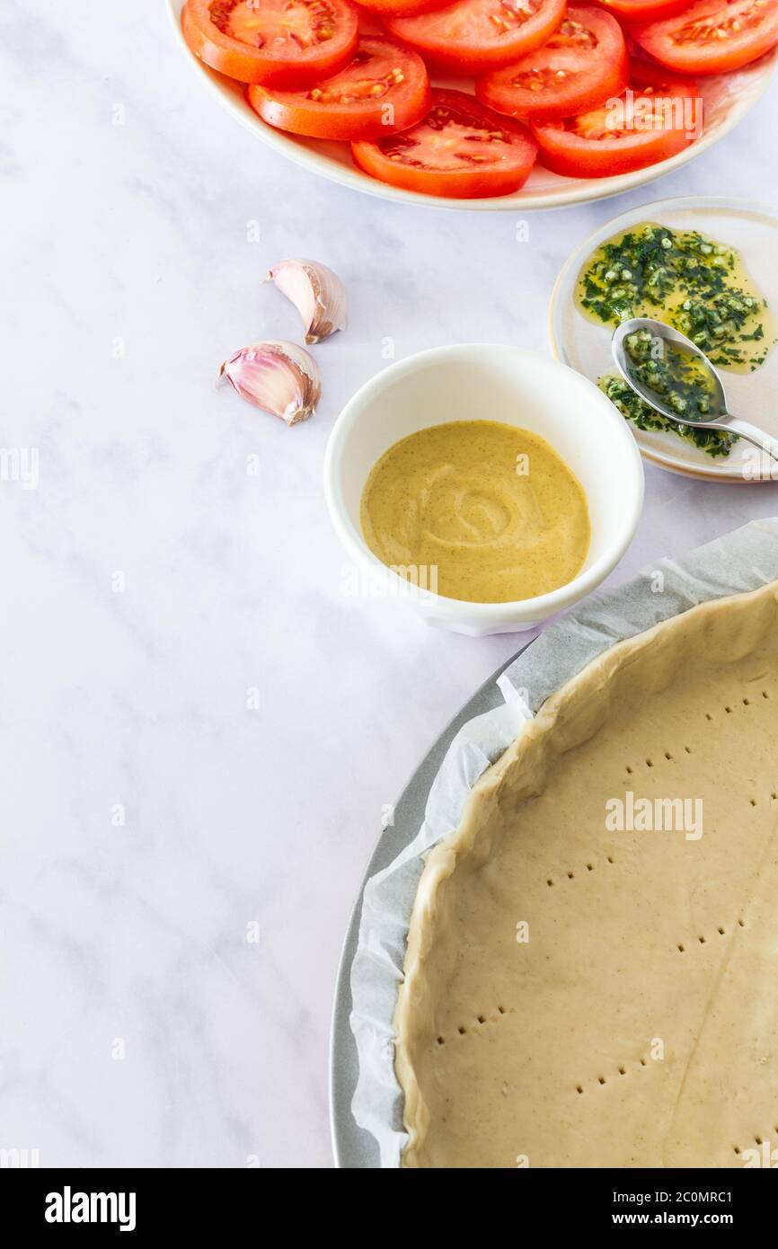 Raw ingredients to make tomato and mustard tart on a white marble backdrop Stock Photo