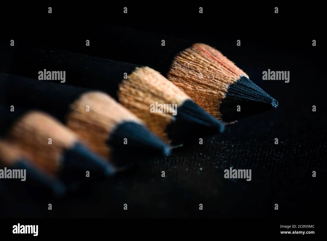A group of pencils are kept on a dark paper in ascending order. Education concept. Selective focus on the tip of the distal pencil Stock Photo