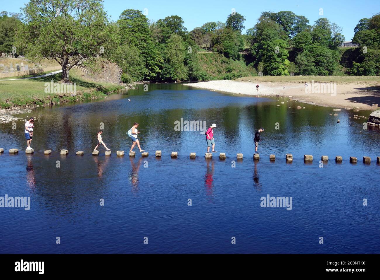 Family Walking on Stepping Stones over the River Wharfe by the Ruins of Bolton Priory, Wharfedale, Yorkshire Dales National Park, England UK. Stock Photo