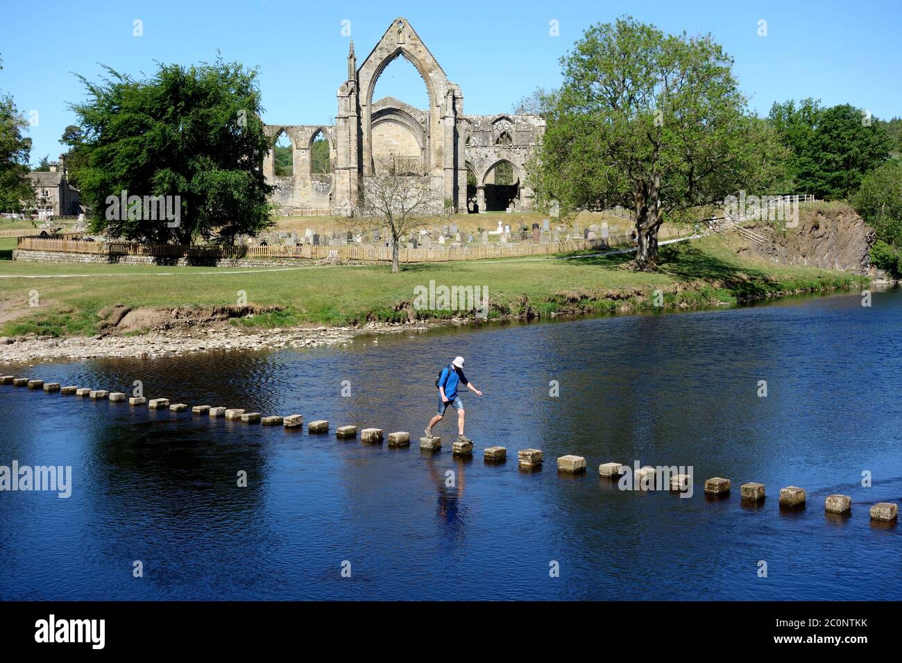 Single Man Walking on Stepping Stones over the River Wharfe by the Ruins of Bolton Priory, Wharfedale, Yorkshire Dales National Park, England UK. Stock Photo