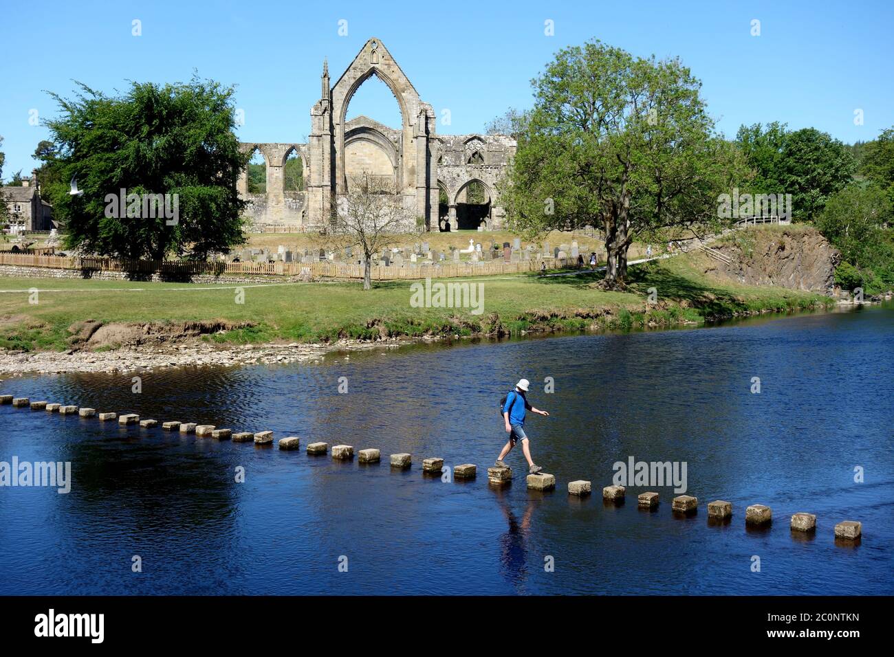 Single Man Walking on Stepping Stones over the River Wharfe by the Ruins of Bolton Priory, Wharfedale, Yorkshire Dales National Park, England UK. Stock Photo