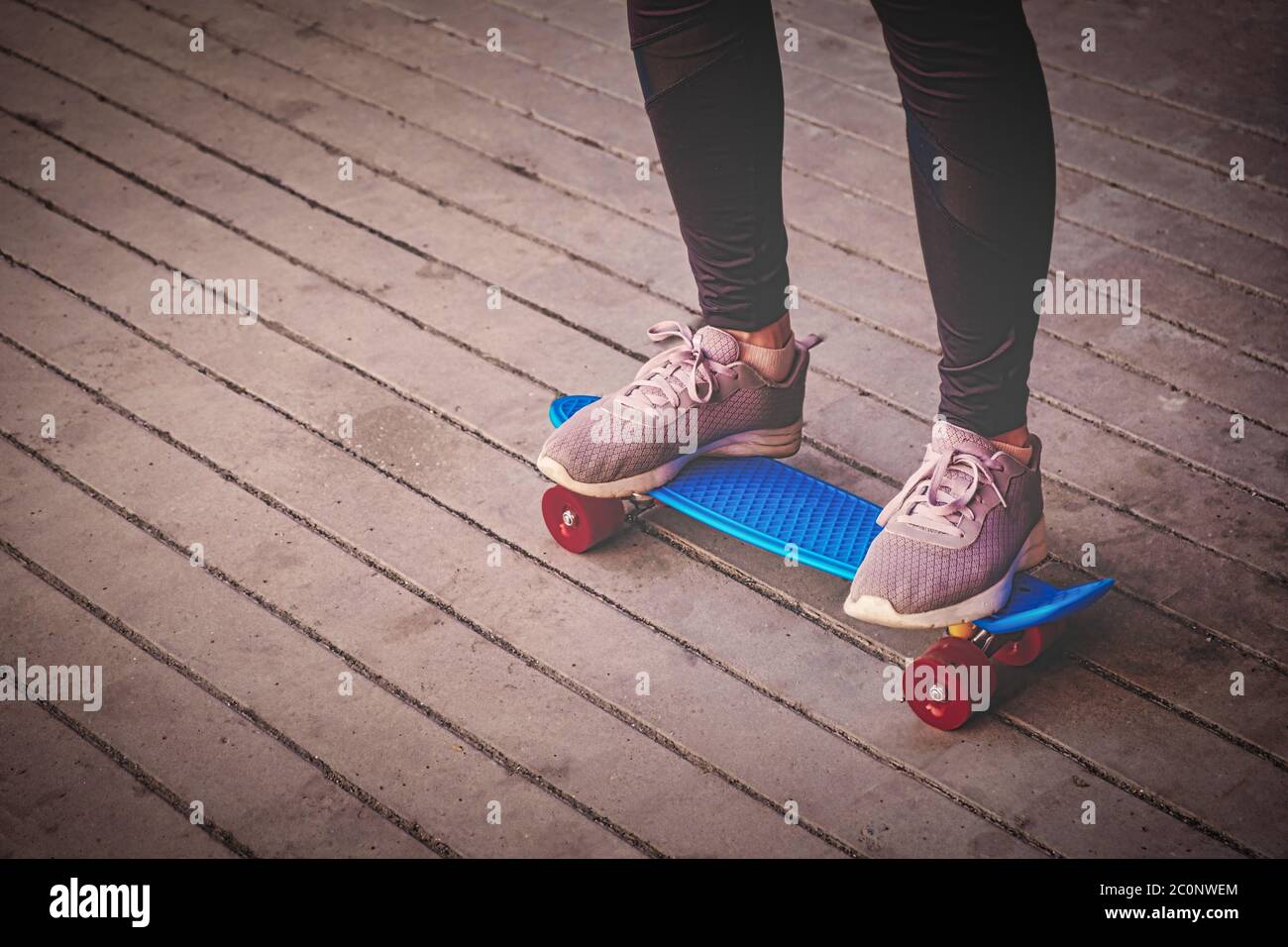 The sporty lady stands on a small blue skateboard, her legs are wearing  leggings and sports shoes Stock Photo - Alamy