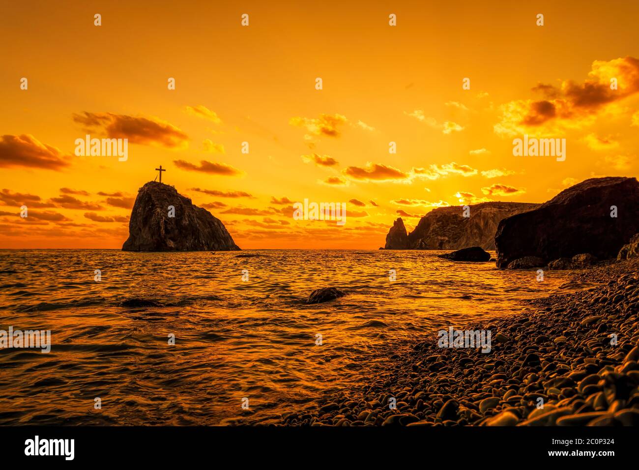 A red burning sunset on pebble beach with the silhouette of a cliff ...