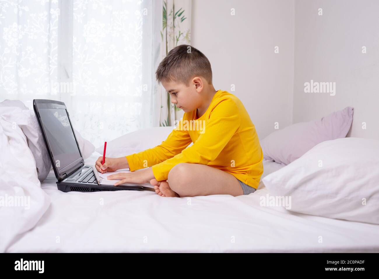 boy doing homework sitting on bed, laptop, handwriting exercise Stock
