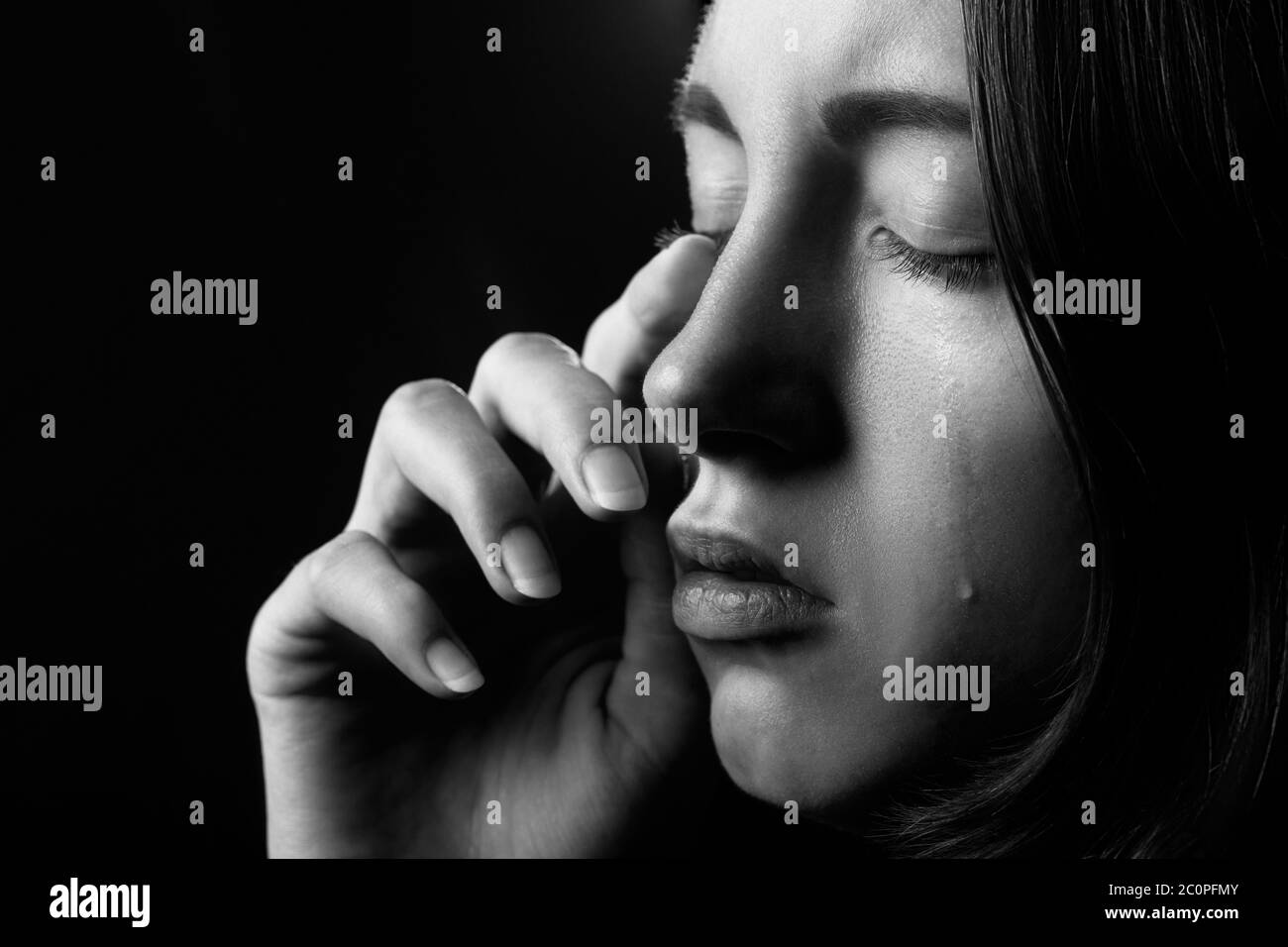 sad woman with closed eyes crying, on black background, closeup portrait, side view, monochrome Stock Photo