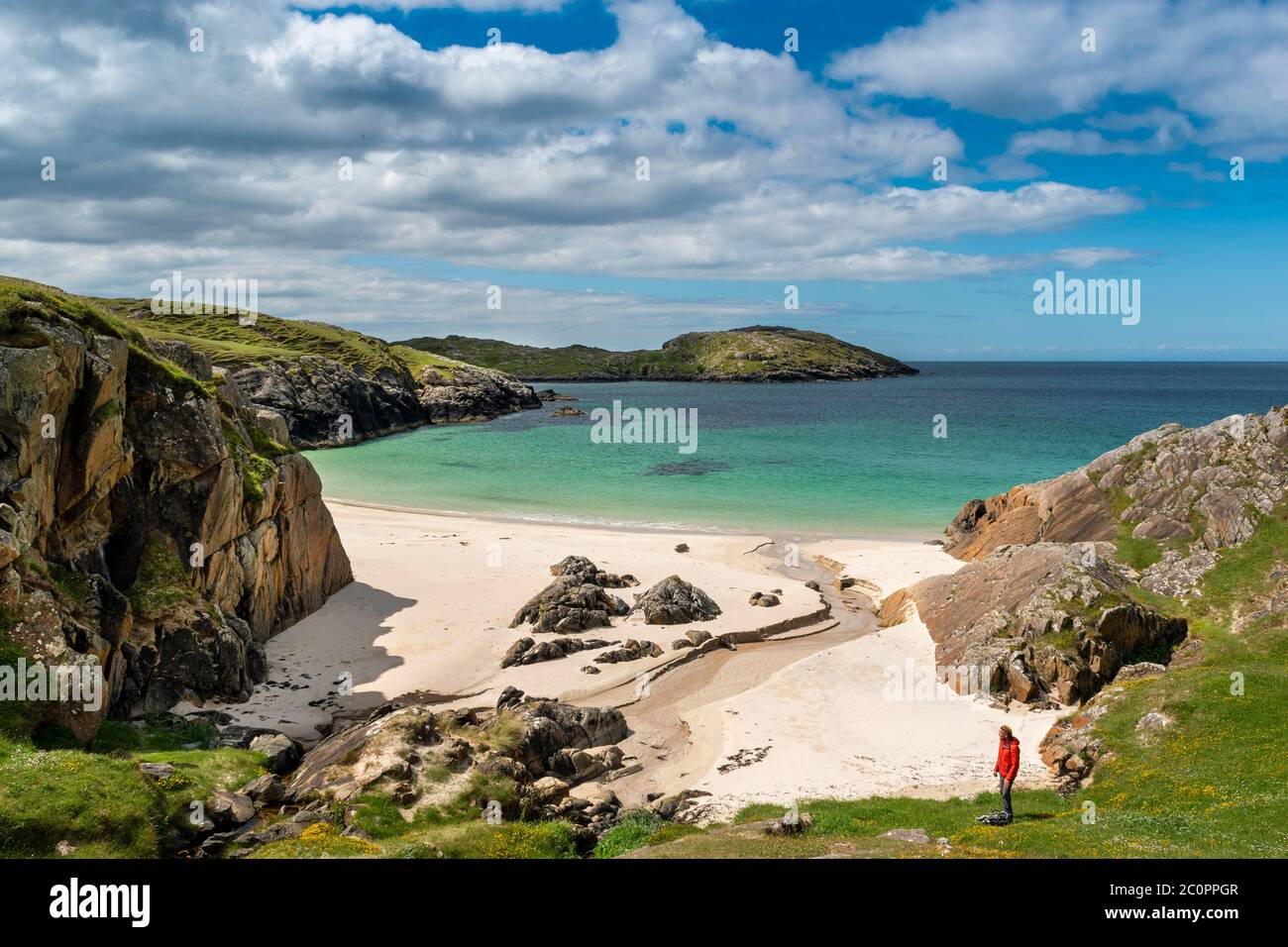 ACHMELVICH BAY AND BEACH SUTHERLAND HIGHLANDS SCOTLAND BLUE  SKY WITH CLOUDS THE MANY COLOURS OF THE SEA AND A LONE HIKER Stock Photo