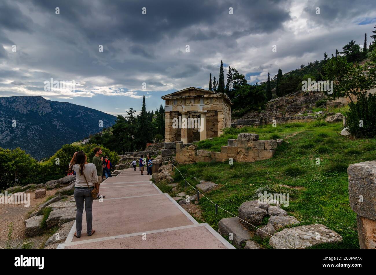 Delphi Town, Phocis / Greece. Tourists are following the Sacred Way at the famous archaeological site of Delphi. Treasure of the Athenians building Stock Photo