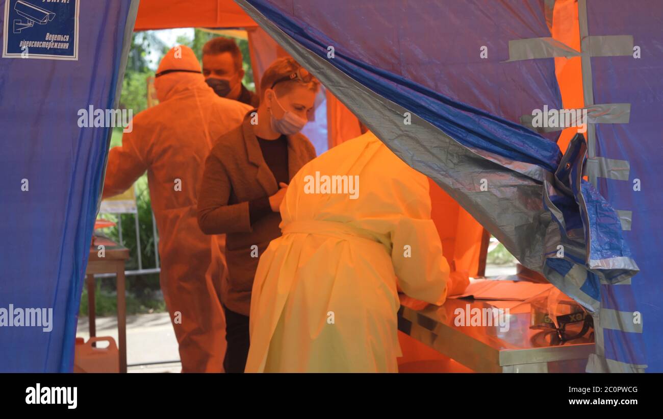 Health workers in suits of epidemiological protection check visitors at entrance to hospital. Abstract defocused image. Centre of counteraction covid Stock Photo