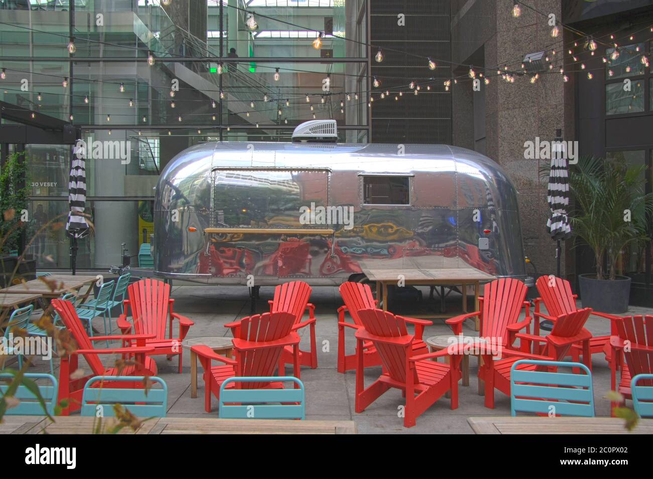 New York City Airstream Metallic caravan cafe business with outdoor seating in front of a glazed facade building in the big apple Stock Photo