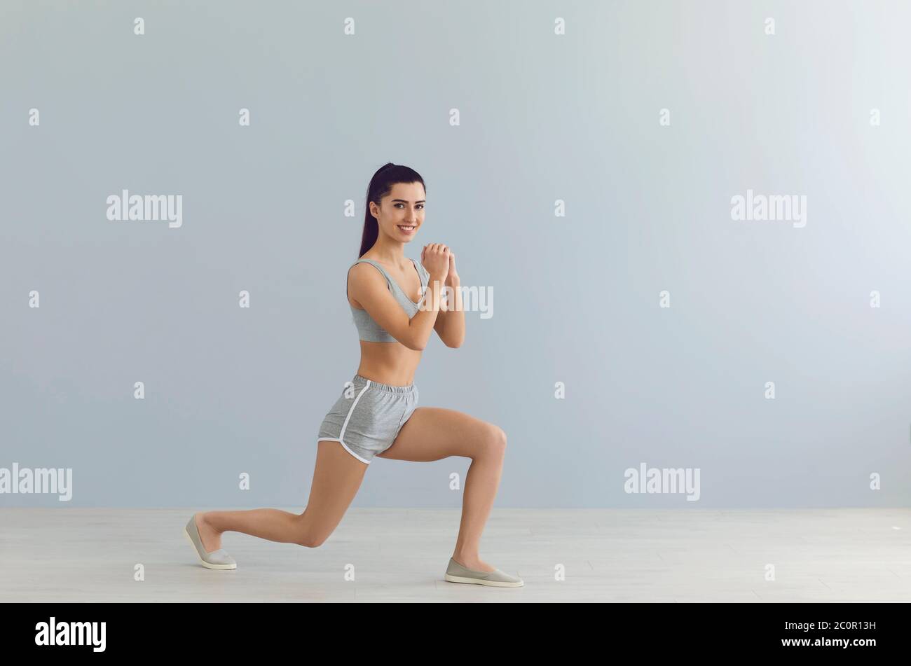 Beautiful smiling girl in sportswear working out on grey background, empty space. Athletic girl doing cardio exercises Stock Photo