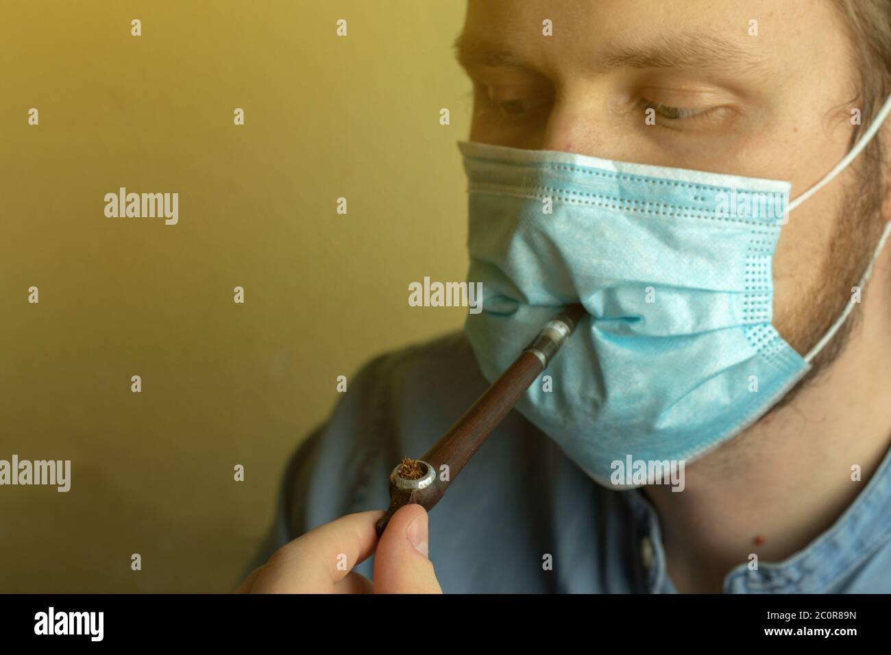 Man wearing mask smoking tobacco with pipe closeup. Face mask. Copy