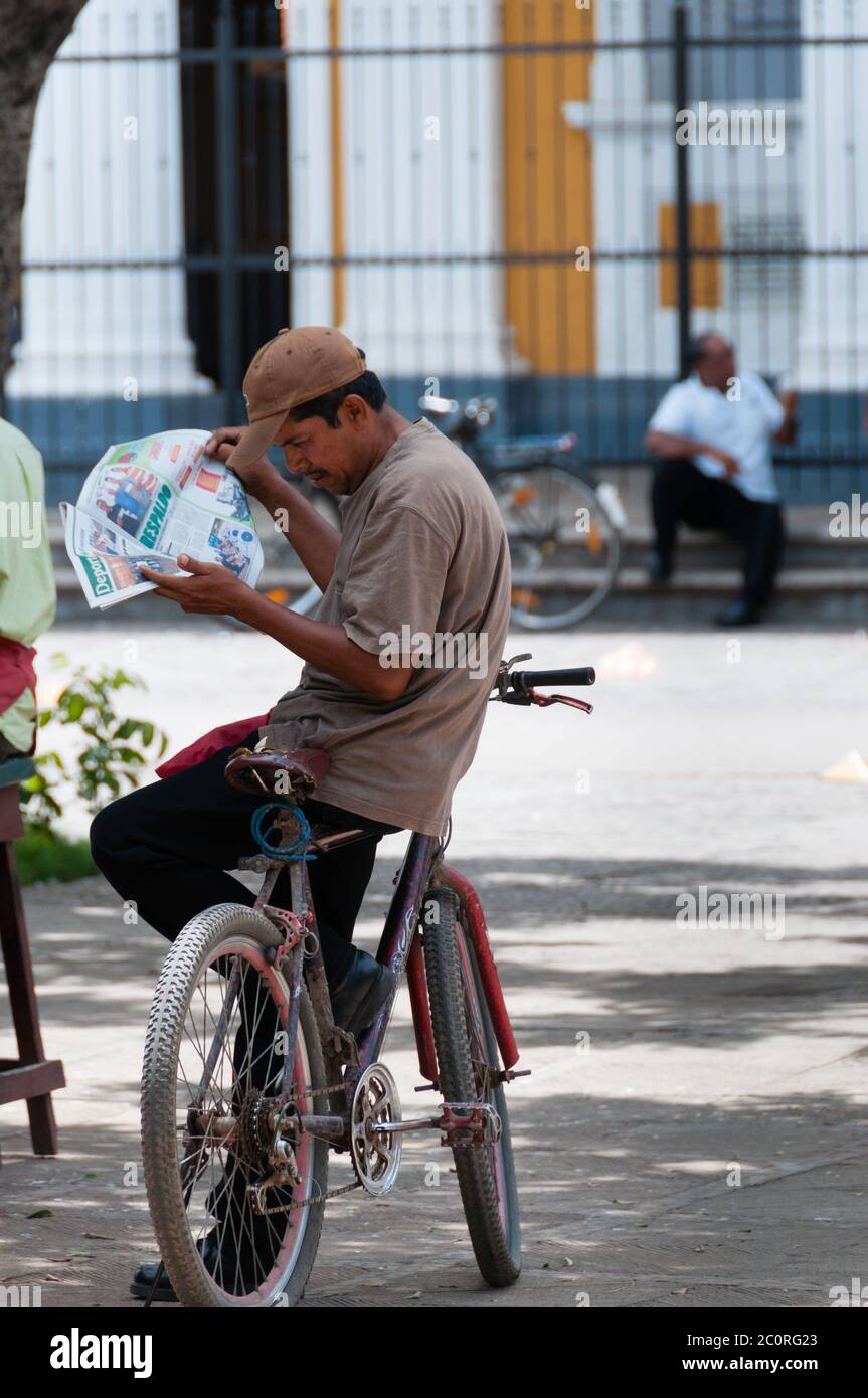 Latin man sitting on bike reading newspaper Stock Photo