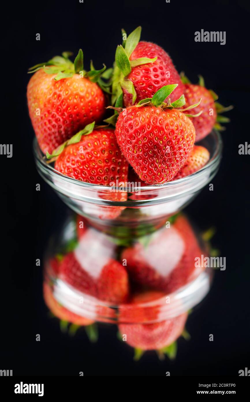 A clear glass bowl of red strawberry with a reflection in a mirrow.  Black background. Stock Photo