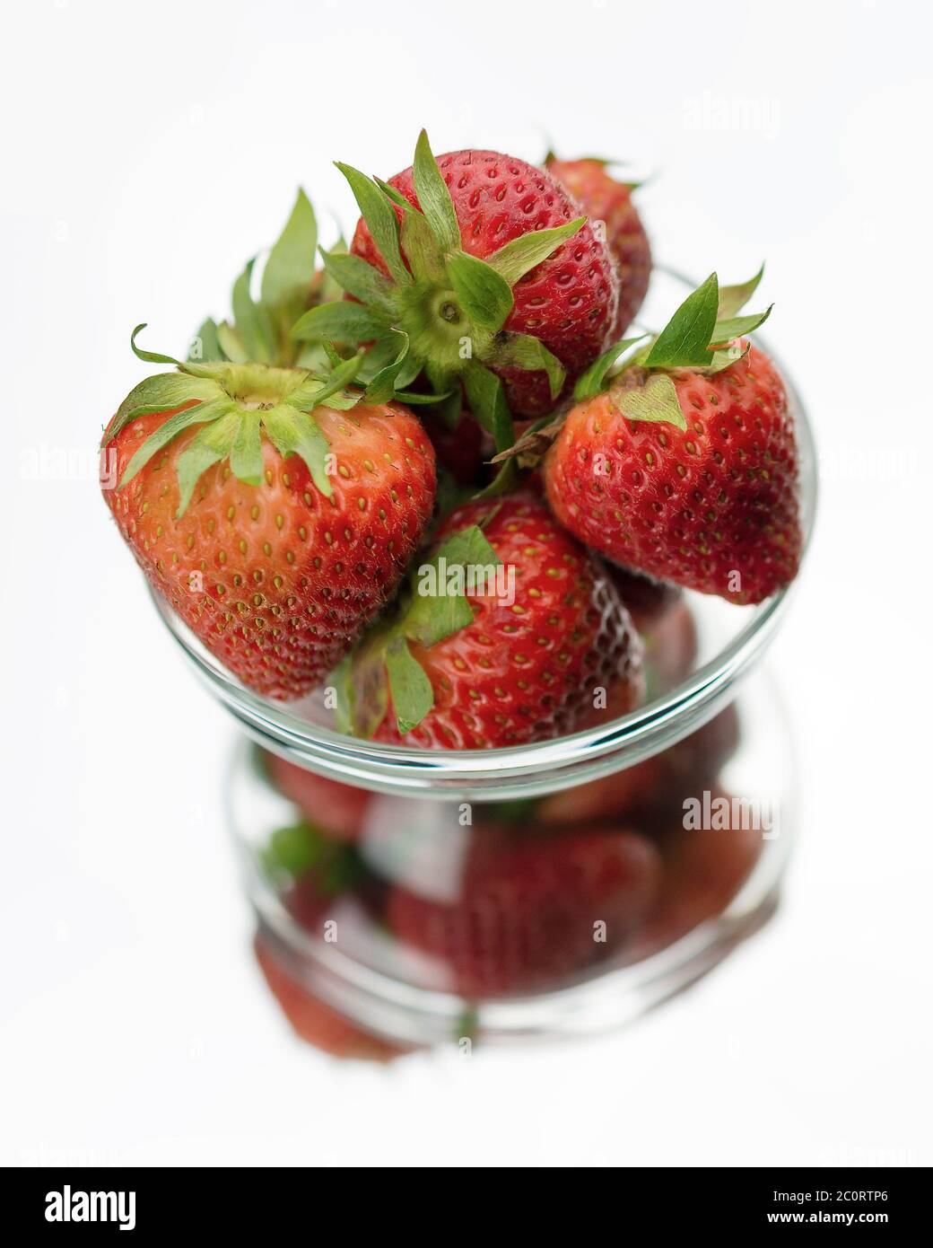 A clear glass bowl of red strawberries with reflection on a mirror.  White background. Stock Photo