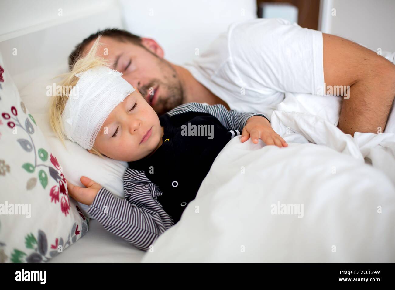 Little toddler boy with head injury, lying with dad in bed, tired