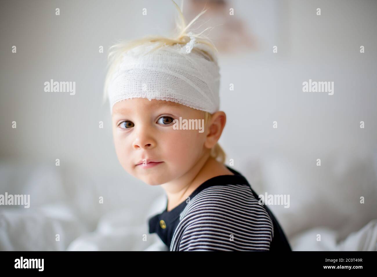 Close portrait of little toddler boy with head injury, sitting in bed