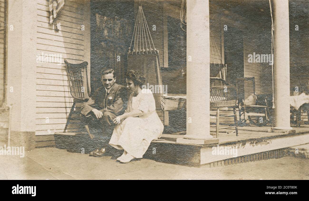 Antique April 1913 photograph, man and woman sitting on porch outside. Exact location unknown, probably New Hampshire or Massachusetts. SOURCE: ORIGINAL PHOTOGRAPH Stock Photo