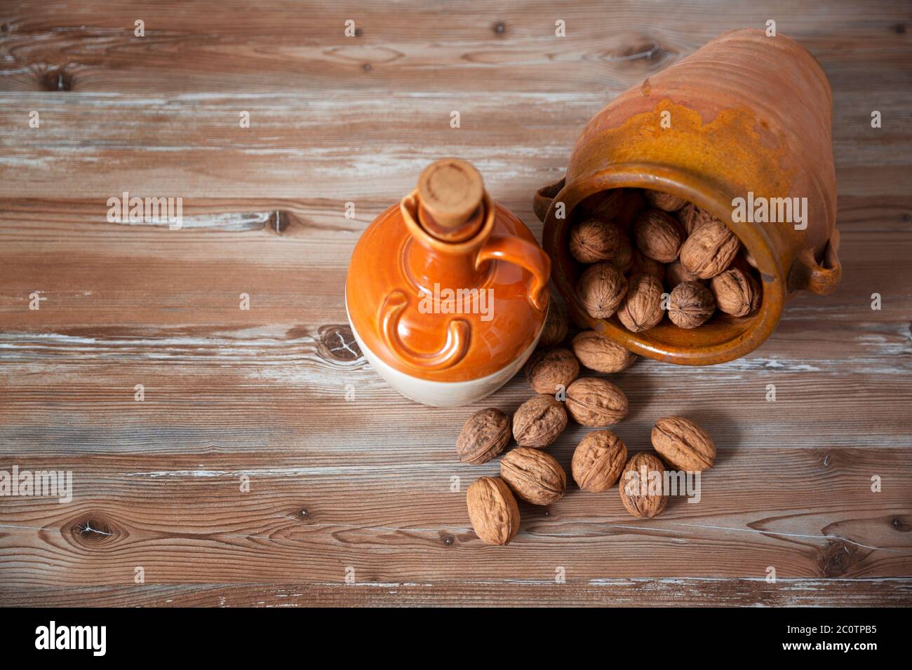 Clay vessel with nuts scattered on aged wooden board. Space for text. Healthy food concept. Stock Photo